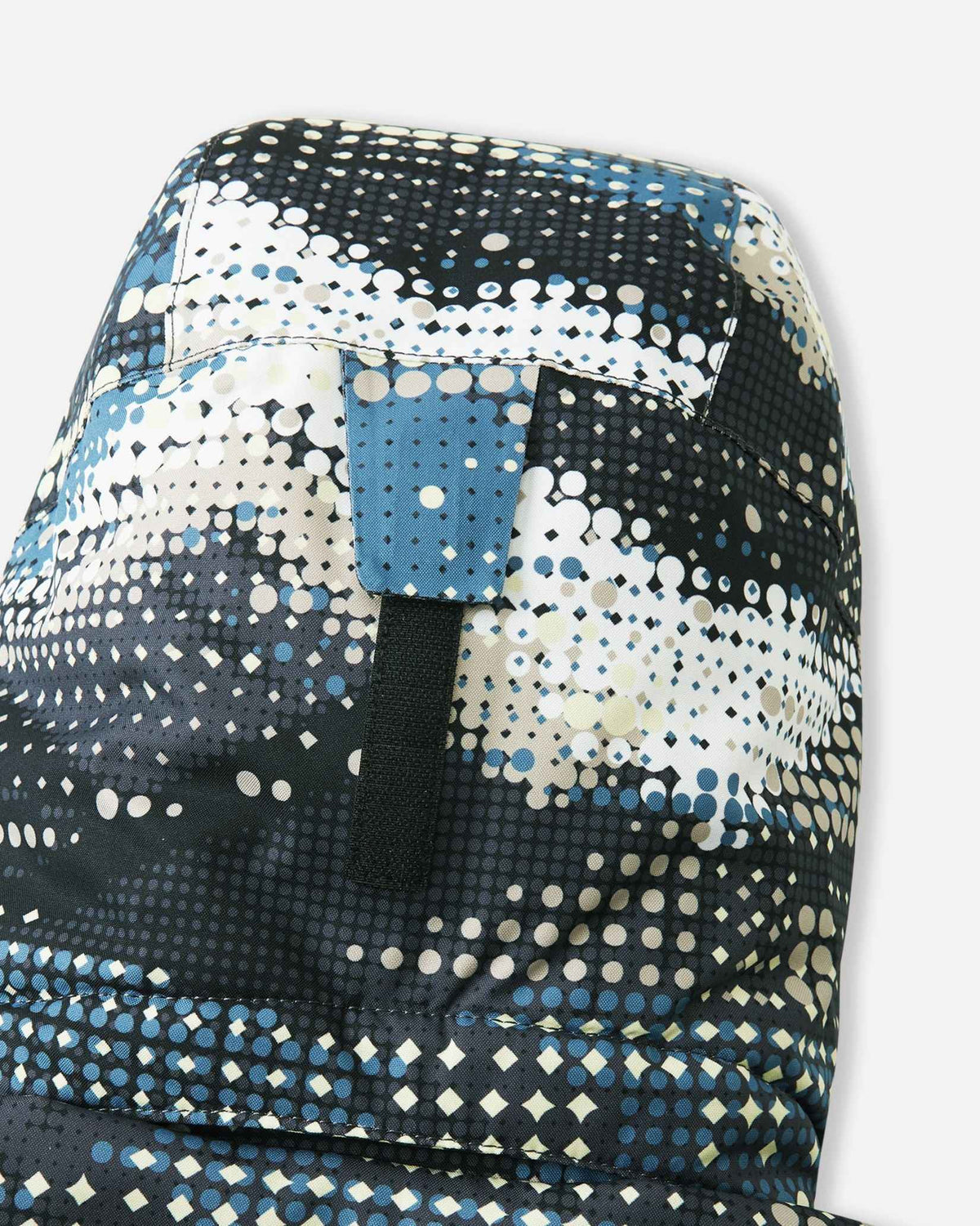 Close-up of the back of the hood on the Reima Lappea kids' ski suit in a soft black, blue, and cream geometric pattern, highlighting the durable velcro adjustment strap that allows parents to customize the fit for safety and helmet compatibility.