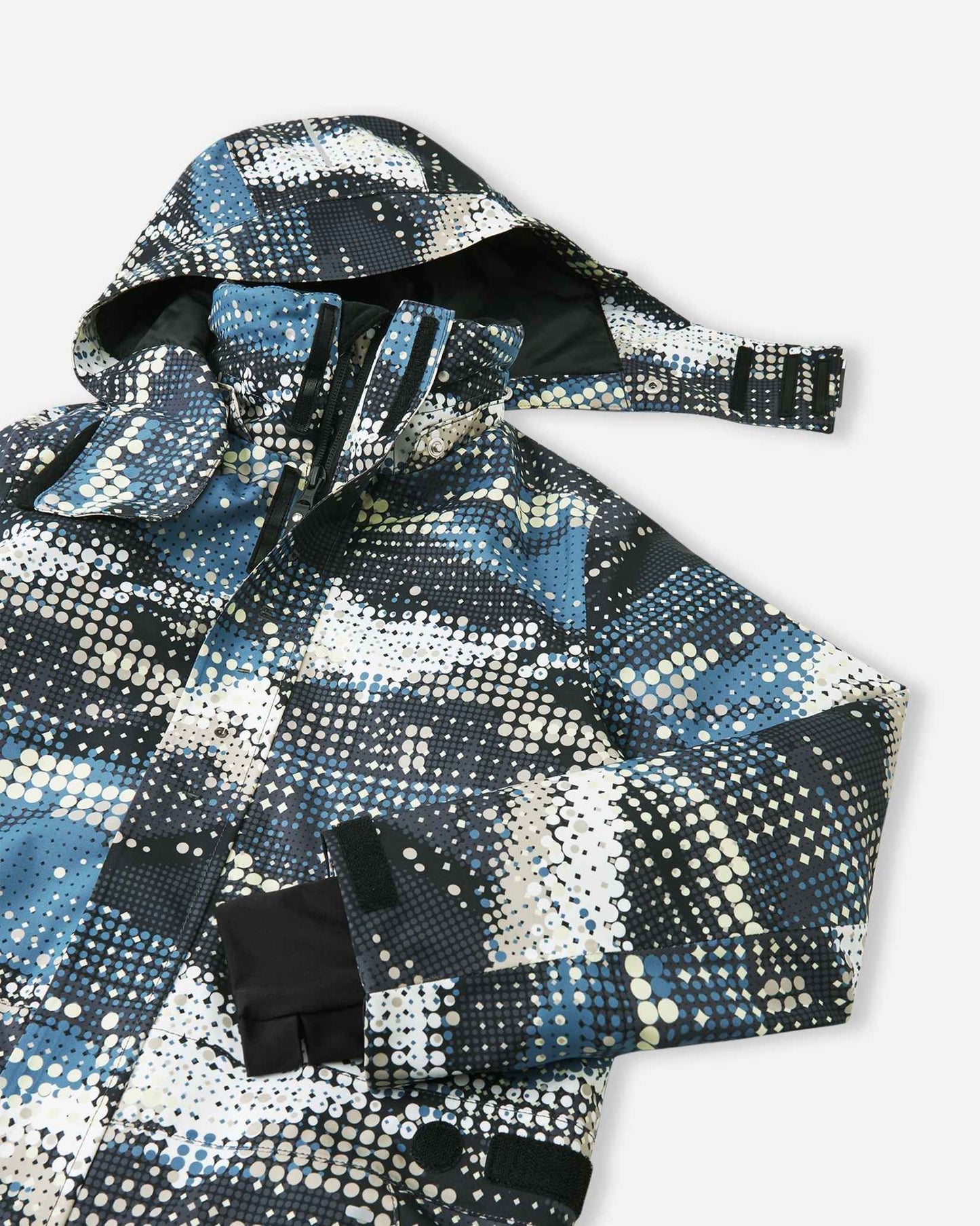 Upper front view of the Reima Lappea kids' winter ski suit showcasing the dynamic soft black, blue, and cream dot pattern, featuring a protective winter hood, a high wind-blocking collar, and a smooth, durable main zipper.