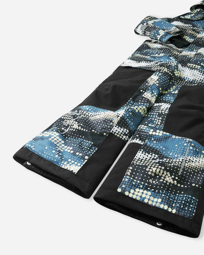Close-up of the lower legs on the Reima Lappea kids' ski suit, showing the transition from solid black durable knee panels to patterned lower legs, complete with reinforced hems and adjustable snap button closures designed to fit securely over ski boots.
