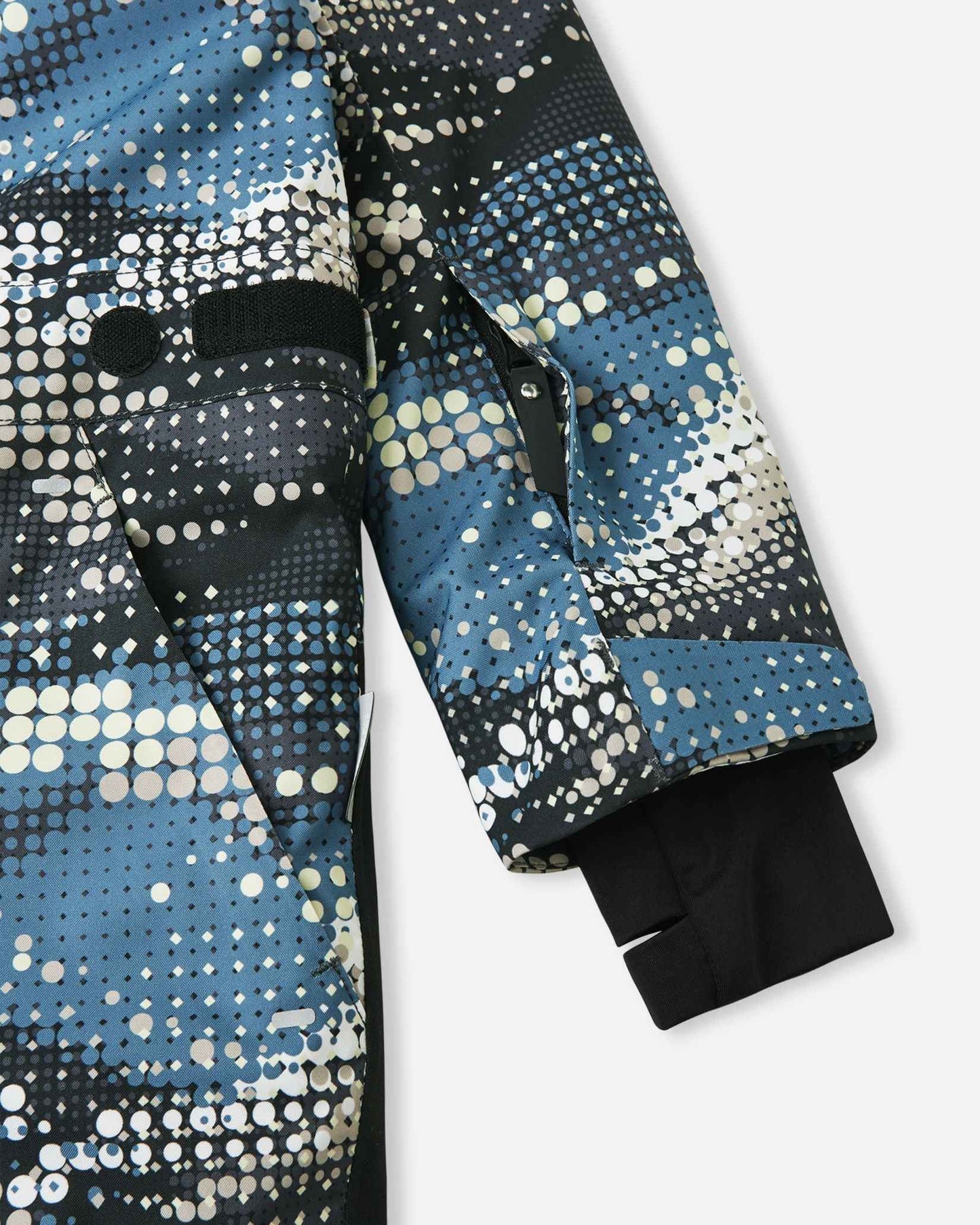 Detail shot of the Reima Lappea kids' ski suit sleeve, featuring a convenient zippered ski pass pocket on the forearm, an adjustable velcro outer cuff, and a cozy inner stretch lycra cuff with a thumb hole to lock out snow and cold drafts.