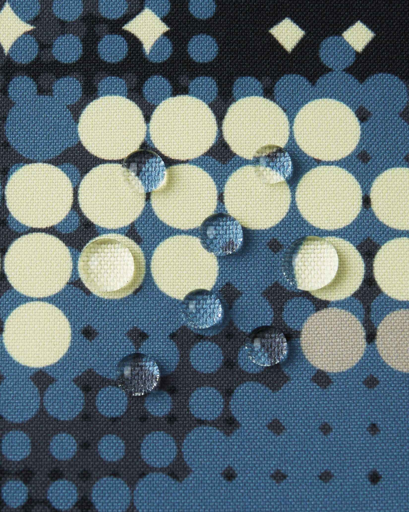 Macro close-up of water droplets tightly beading on the patterned Reimatec fabric of the Reima Lappea kids' ski suit, demonstrating its highly waterproof and moisture-resistant properties designed for active winter snow sports.