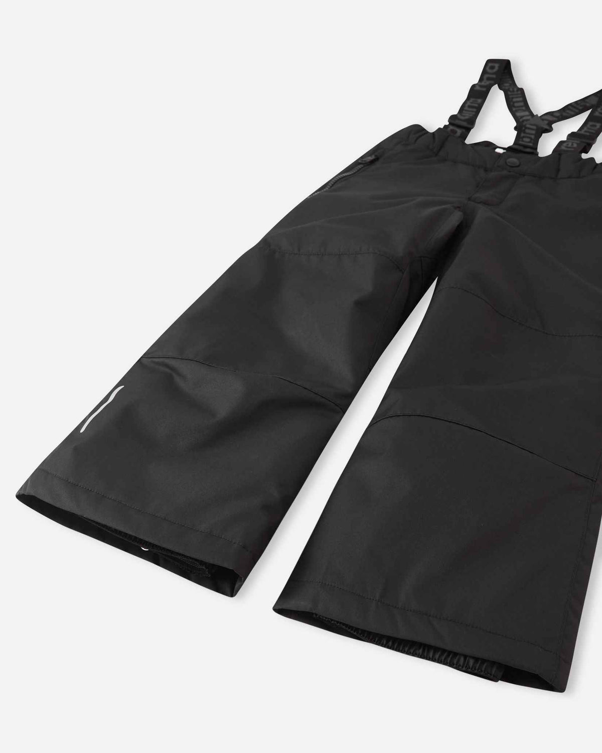 Detail view of the lower legs on the black Reima Liikun kids' snow pants, emphasizing the rugged reinforced hems to protect against wear and the inner elastic snow locks designed to securely grip winter boots.