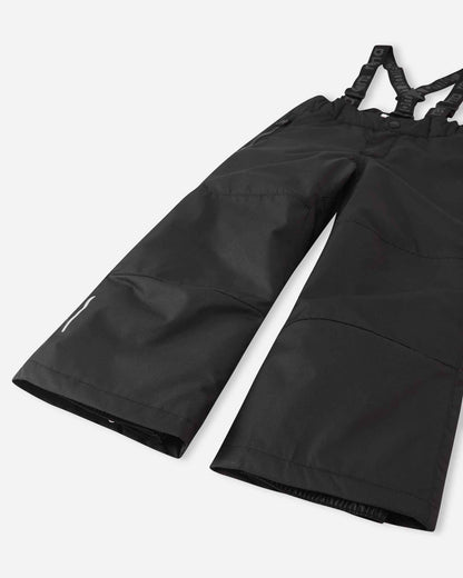 Detail view of the lower legs on the black Reima Liikun kids' snow pants, emphasizing the rugged reinforced hems to protect against wear and the inner elastic snow locks designed to securely grip winter boots.