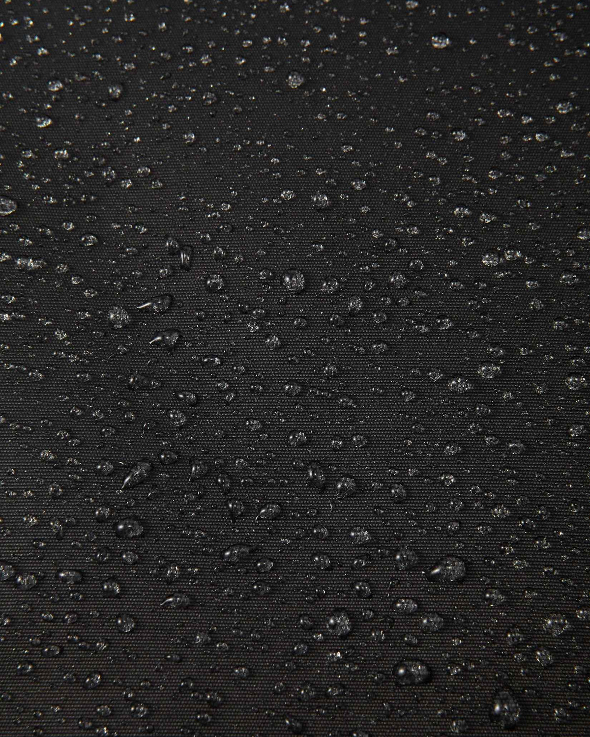 Macro close-up of water droplets actively beading and rolling off the black outer shell of the Reima Liikun kids' snow pants, visually highlighting the high-performance breathable and waterproof Reimatec technology.