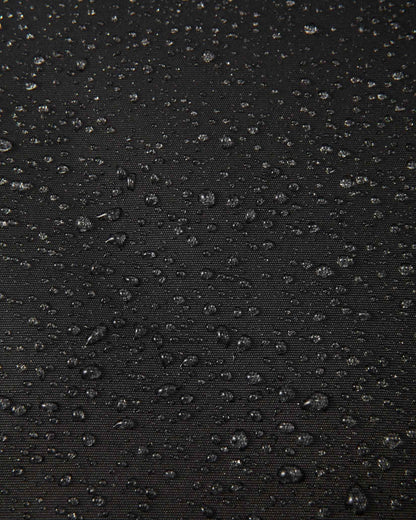 Macro close-up of water droplets actively beading and rolling off the black outer shell of the Reima Liikun kids' snow pants, visually highlighting the high-performance breathable and waterproof Reimatec technology.