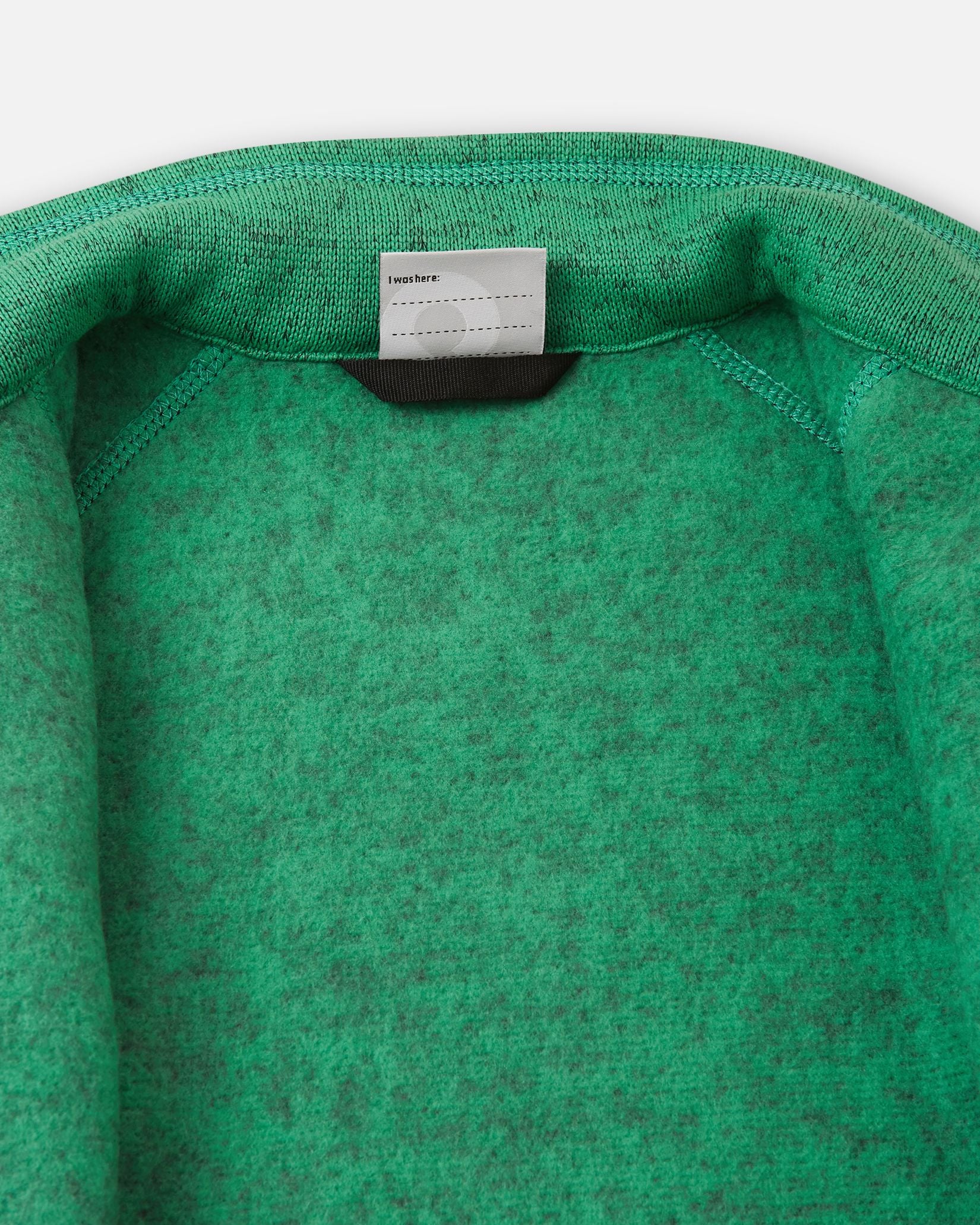 Inside collar view of the green Reima Liukuen kids' fleece jacket, displaying the soft brushed fleece interior for thermal comfort and a customizable name tag.