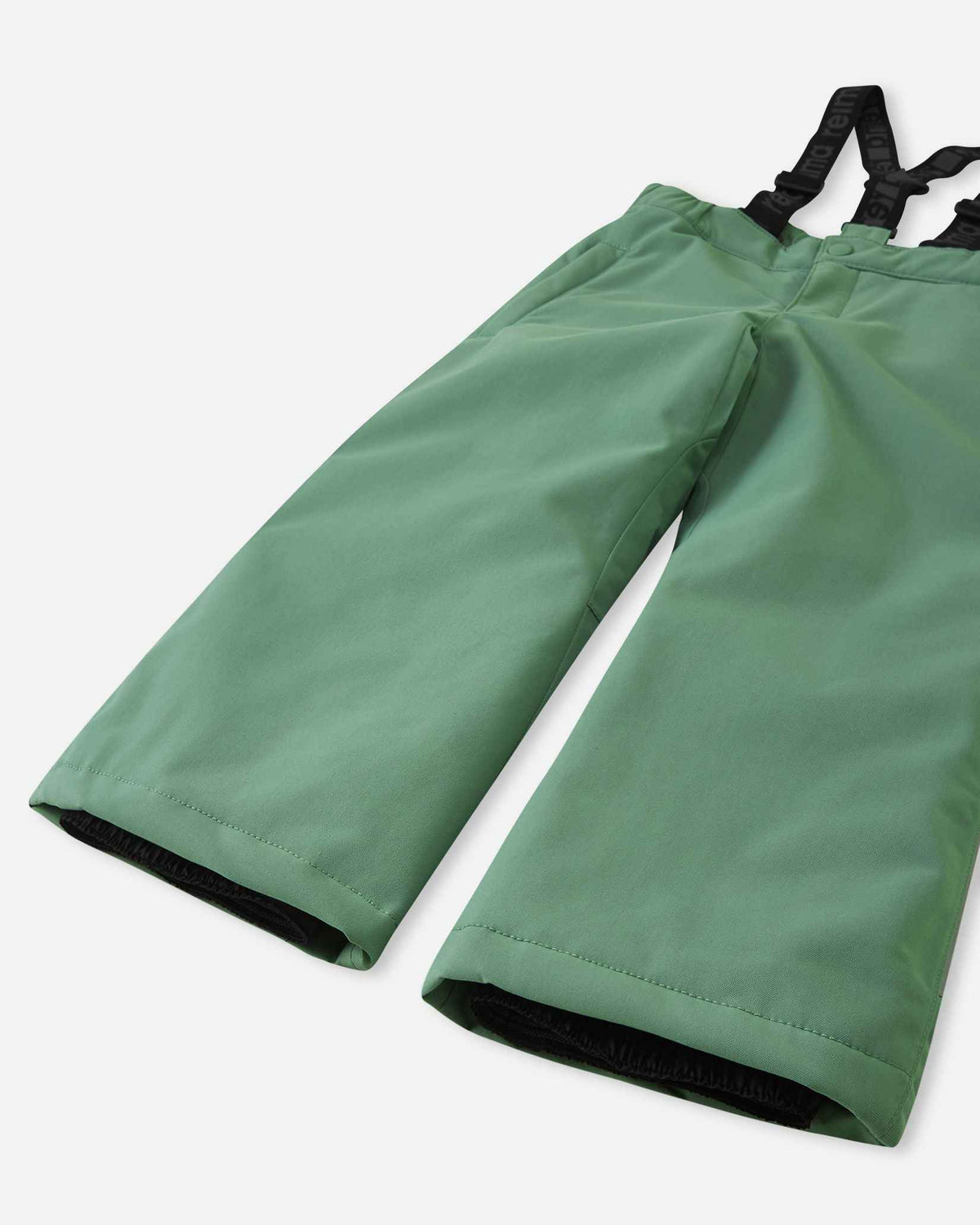 Detail view of the lower legs on the green clay Reima Loikin kids' snow pants, emphasizing the rugged reinforced hems to protect against wear and the inner elastic snow locks designed to securely grip winter boots.