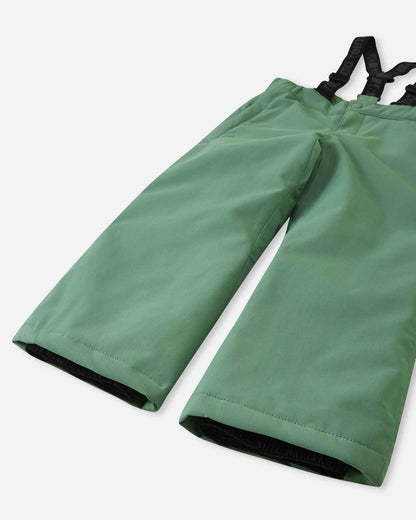 Detail view of the lower legs on the green clay Reima Loikin kids' snow pants, emphasizing the rugged reinforced hems to protect against wear and the inner elastic snow locks designed to securely grip winter boots.