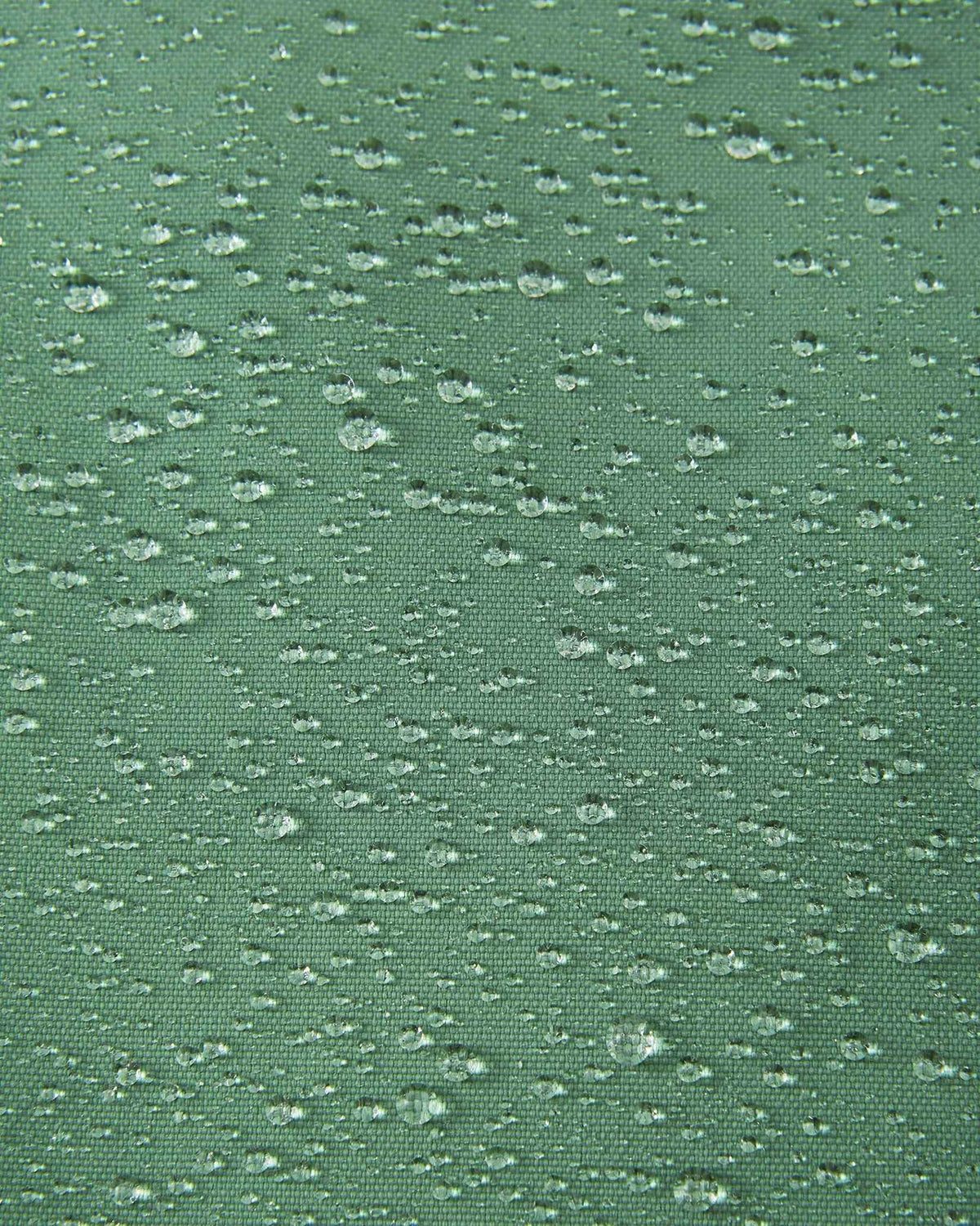 Macro close-up of water droplets actively beading and rolling off the green clay outer shell of the Reima Loikin kids' snow pants, visually highlighting the high-performance breathable and waterproof Reimatec technology.