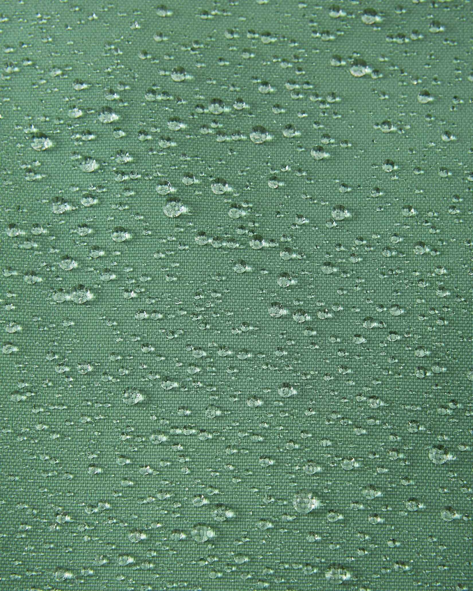 Macro close-up of water droplets actively beading and rolling off the green clay outer shell of the Reima Loikin kids' snow pants, visually highlighting the high-performance breathable and waterproof Reimatec technology.