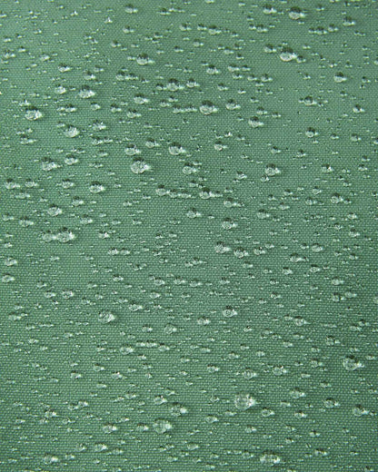 Macro close-up of water droplets actively beading and rolling off the green clay outer shell of the Reima Loikin kids' snow pants, visually highlighting the high-performance breathable and waterproof Reimatec technology.