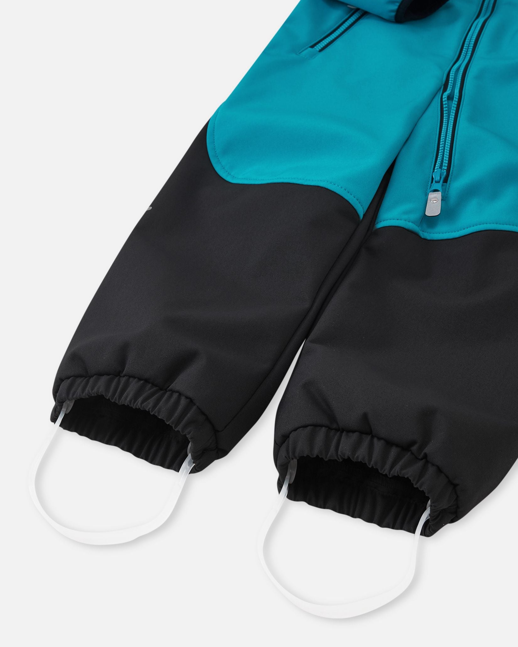 Detailed close-up of the gathered elastic ankle cuffs and durable silicone stirrup foot loops on the aquatic blue Reima Mjosa kids' softshell suit to prevent riding up during play.