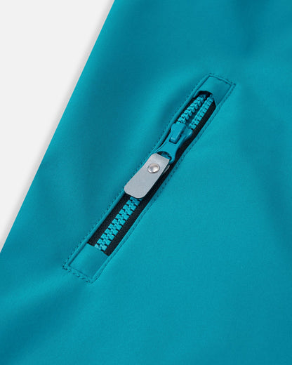 Close-up of the functional zippered chest pocket on the aquatic blue Reima Mjosa kids' softshell suit, highlighting the color-matched aquatic zipper and clean stitching.