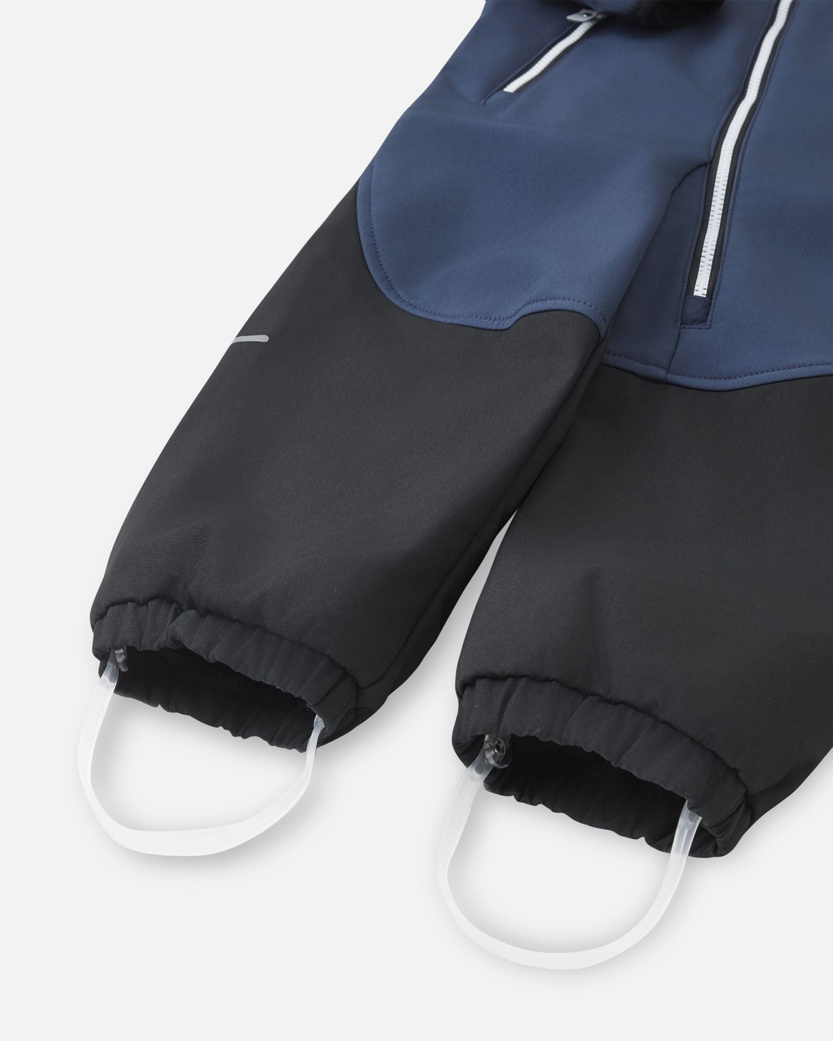 Detailed close-up of the gathered elastic ankle cuffs and durable silicone stirrup foot loops on the navy Reima Mjosa kids' softshell suit, designed to keep pant legs securely over boots.