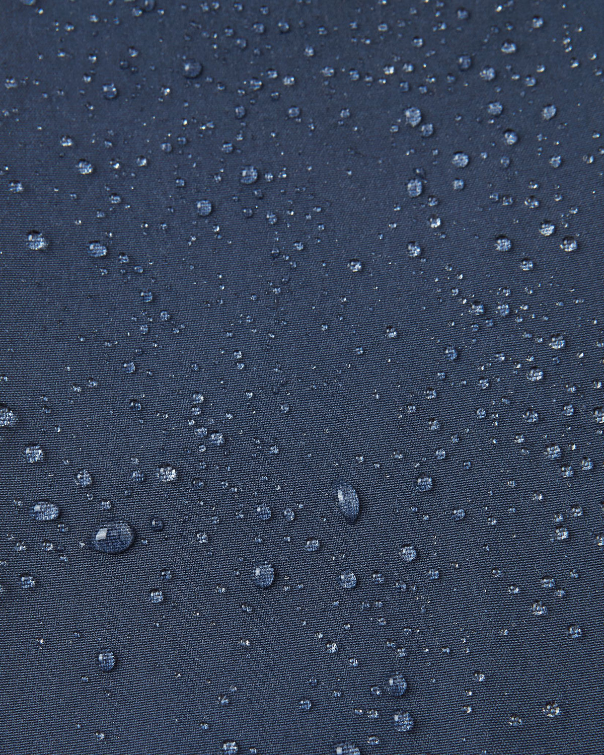 Macro close-up of water droplets beading and rolling off the surface of the navy blue Reima Mjosa kids' softshell suit, demonstrating the highly waterproof and dirt-repellent material.