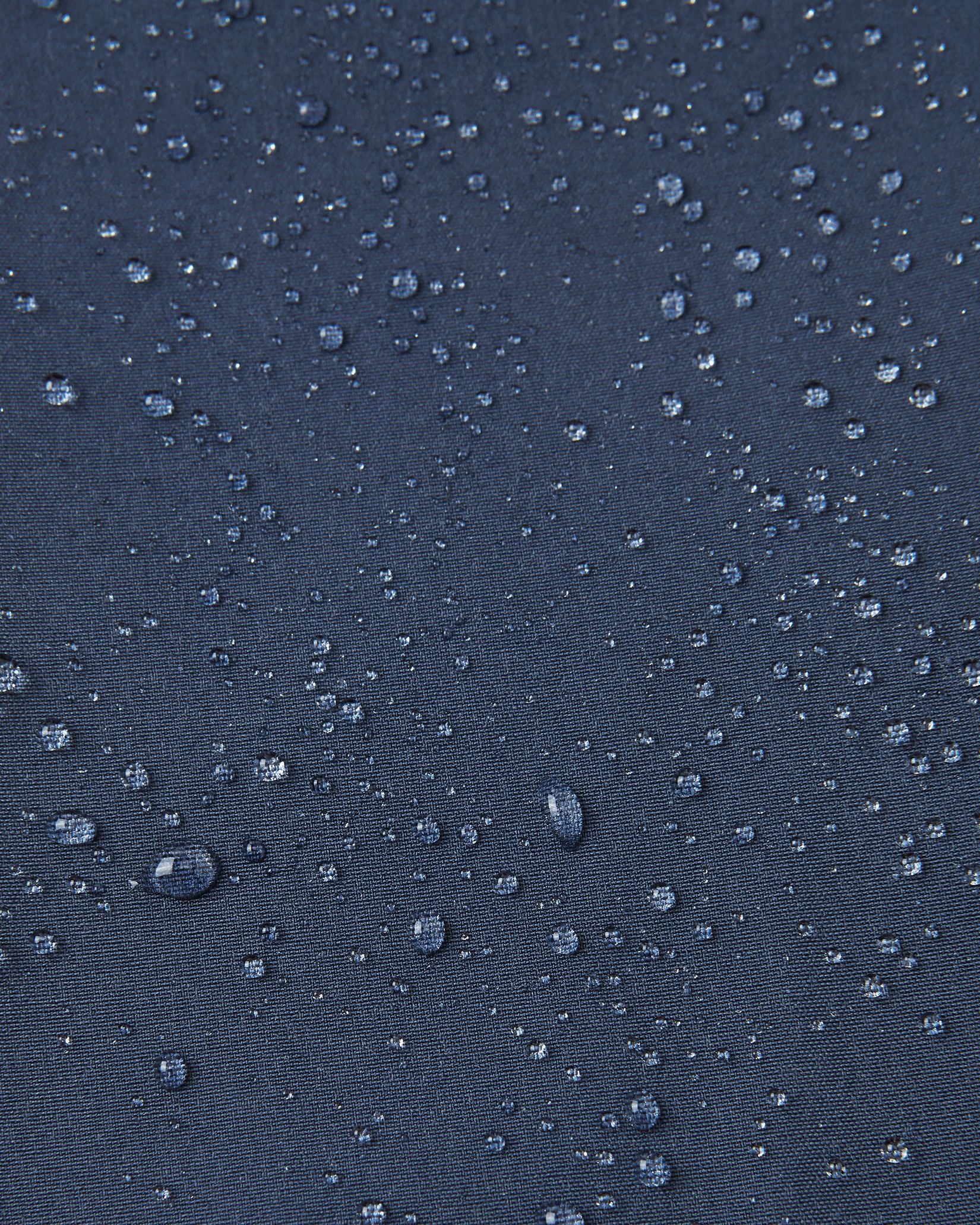 Macro close-up of water droplets beading and rolling off the surface of the navy blue Reima Mjosa kids' softshell suit, demonstrating the highly waterproof and dirt-repellent material.