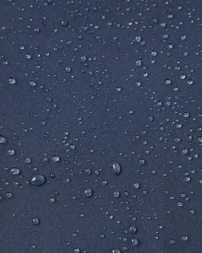 Macro close-up of water droplets beading and rolling off the surface of the navy blue Reima Mjosa kids' softshell suit, demonstrating the highly waterproof and dirt-repellent material.