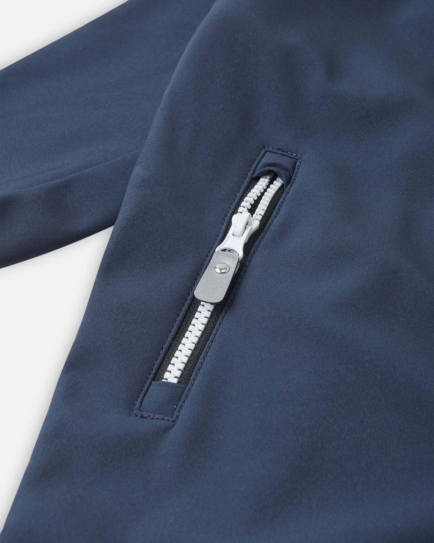 Detail view of the secure zippered pocket on the navy Reima Mjosa kids' softshell coverall, featuring a grey pull tab and clean, weather-resistant trimming.