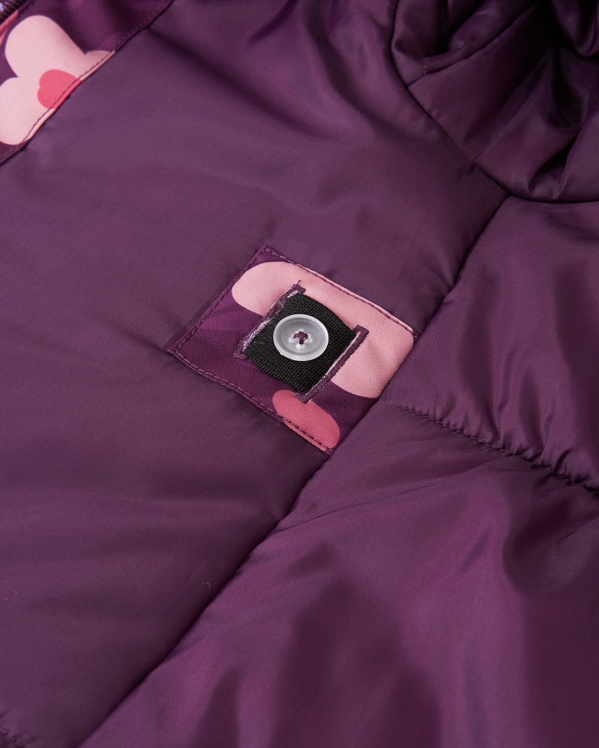 Close-up of the interior lining of the Reima Muurame girls' jacket, showing the internal button and elastic system that allows parents to cinch the waist for a tailored, snug fit.