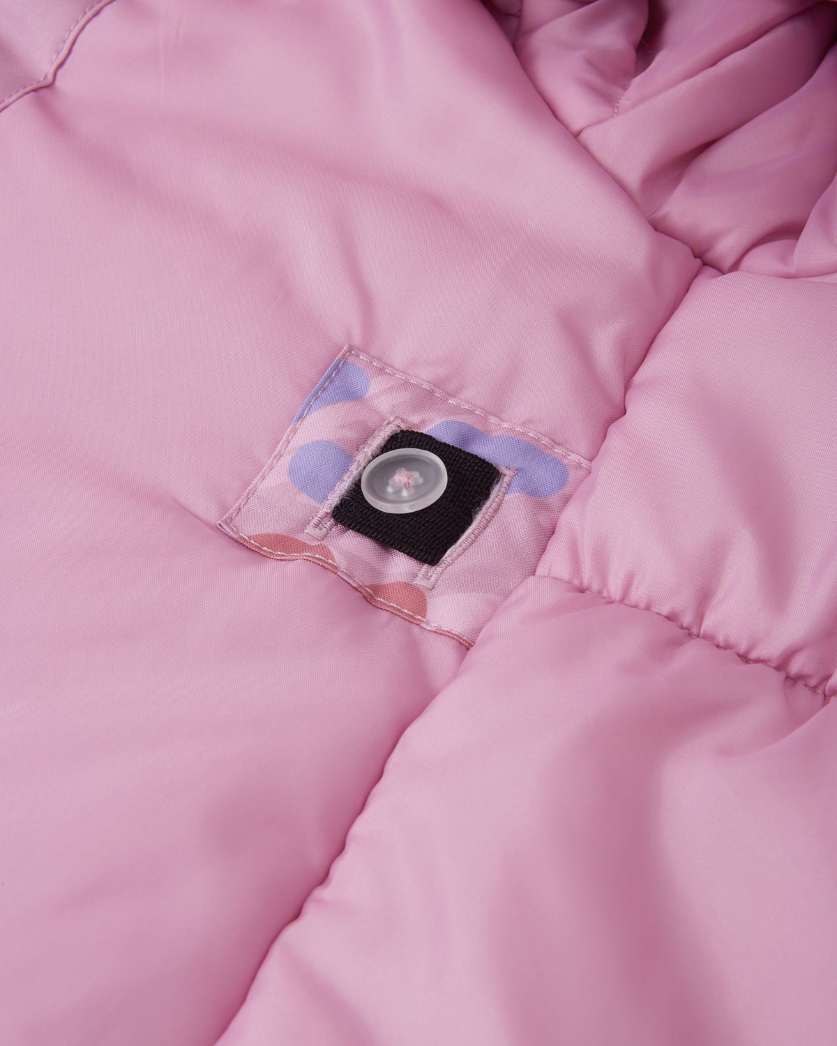 Close-up of the interior lining of the Reima Muurame girls' winter jacket, featuring an internal button and elastic system that allows parents to adjust the waist for a tailored, snug fit.