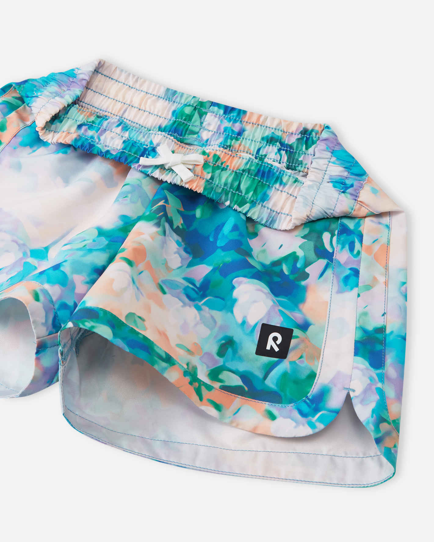 Detailed close-up of the Reima Nauru girls' fresh blue floral swim shorts, highlighting the comfortable smocked elastic waistband and secure inner white drawstring for an adjustable fit.