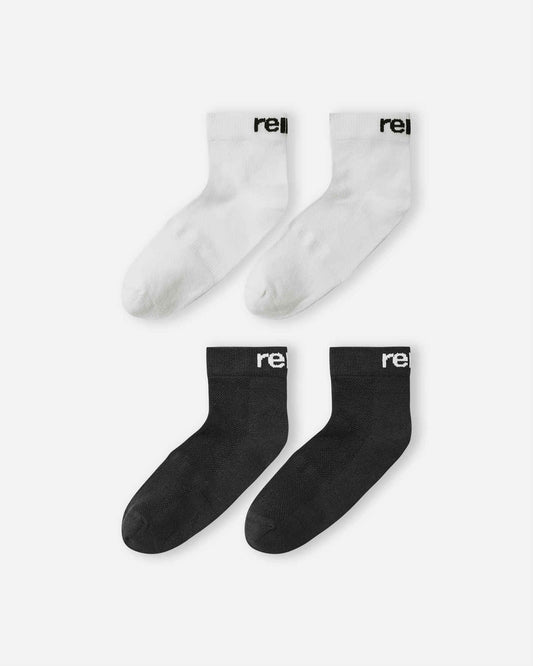 Flat lay view of the Reima Nilkat kids' ankle socks 2-pack, featuring one pair in solid black and one pair in solid white, designed with comfortable ribbed cuffs and the Reima logo for everyday wear.