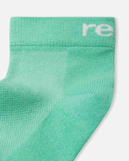 Flat lay view of the Reima Nilkat kids' ankle socks 2-pack, featuring one pair in a vibrant fresh mint green and one pair in classic white, crafted from a breathable cotton blend.