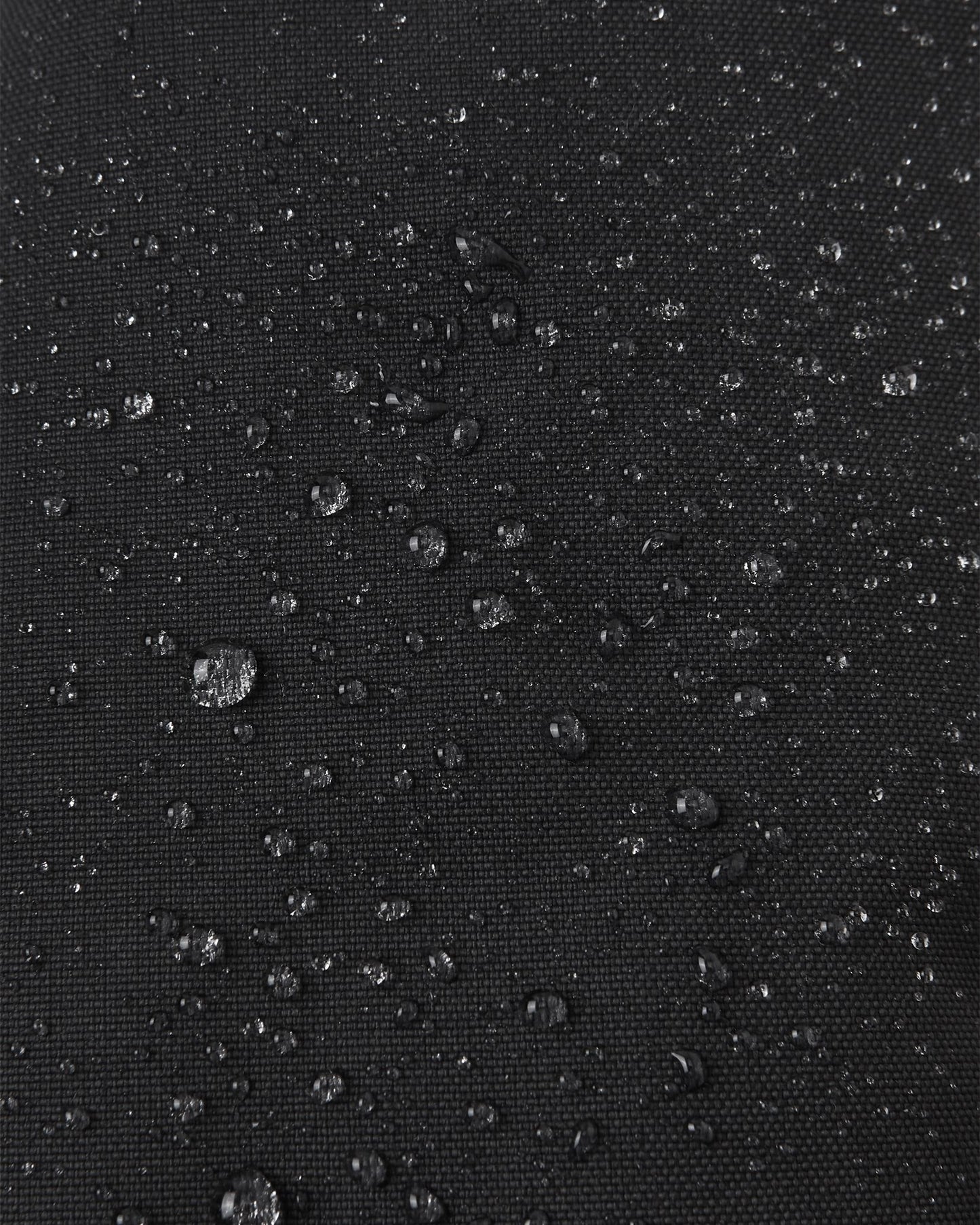 Macro close-up of water droplets beading tightly on the black Reimatec waterproof fabric of the Reima Ote kids' winter mittens, demonstrating superior snow and moisture resistance.