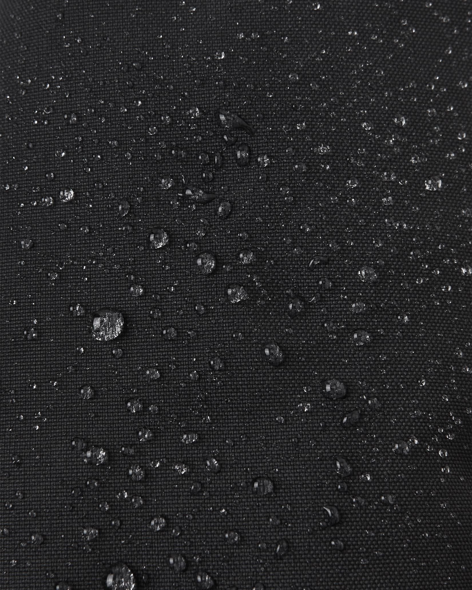 Macro close-up of water droplets beading tightly on the black Reimatec waterproof fabric of the Reima Ote kids' winter mittens, demonstrating superior snow and moisture resistance.