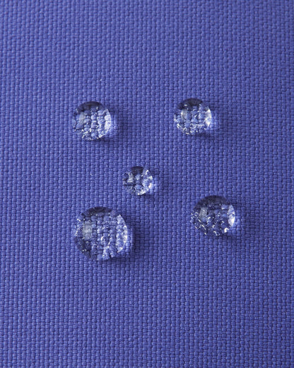Macro close-up of water droplets beading tightly on the breezy violet Reimatec waterproof fabric of the Reima Ote kids' winter mittens, highlighting exceptional snow and moisture resistance.