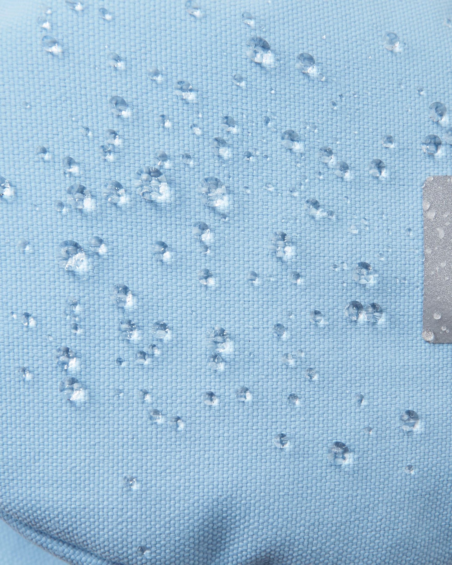 Macro close-up of water droplets beading tightly on the frozen blue Reimatec fabric of the Reima Ote kids' winter mittens, demonstrating extreme waterproof and weather-resistant performance for heavy snow play.