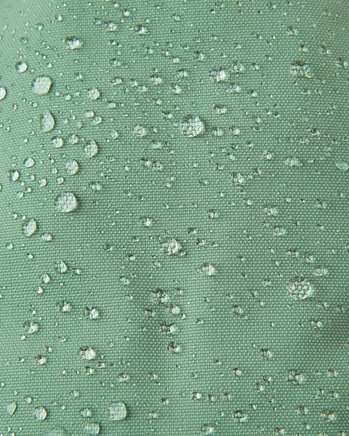 Macro close-up of water droplets beading tightly on the green clay Reimatec fabric of the Reima Ote kids' winter mittens, demonstrating extreme waterproof and weather-resistant performance for snow play.