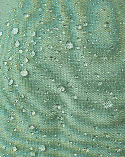 Macro close-up of water droplets beading tightly on the green clay Reimatec fabric of the Reima Ote kids' winter mittens, demonstrating extreme waterproof and weather-resistant performance for snow play.