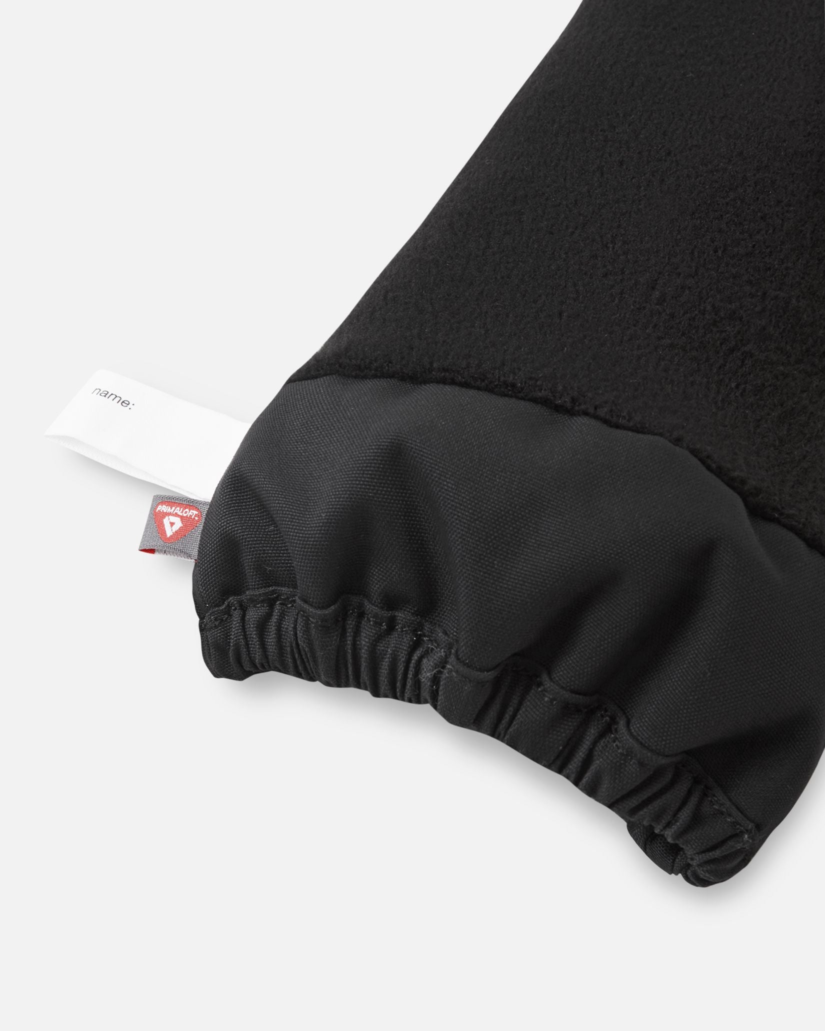 Inside cuff view of the black Reima Ote kids' winter mittens, highlighting the warm fleece lining, a customizable inner name tag, and a PrimaLoft insulation tag for maximum cold-weather warmth.