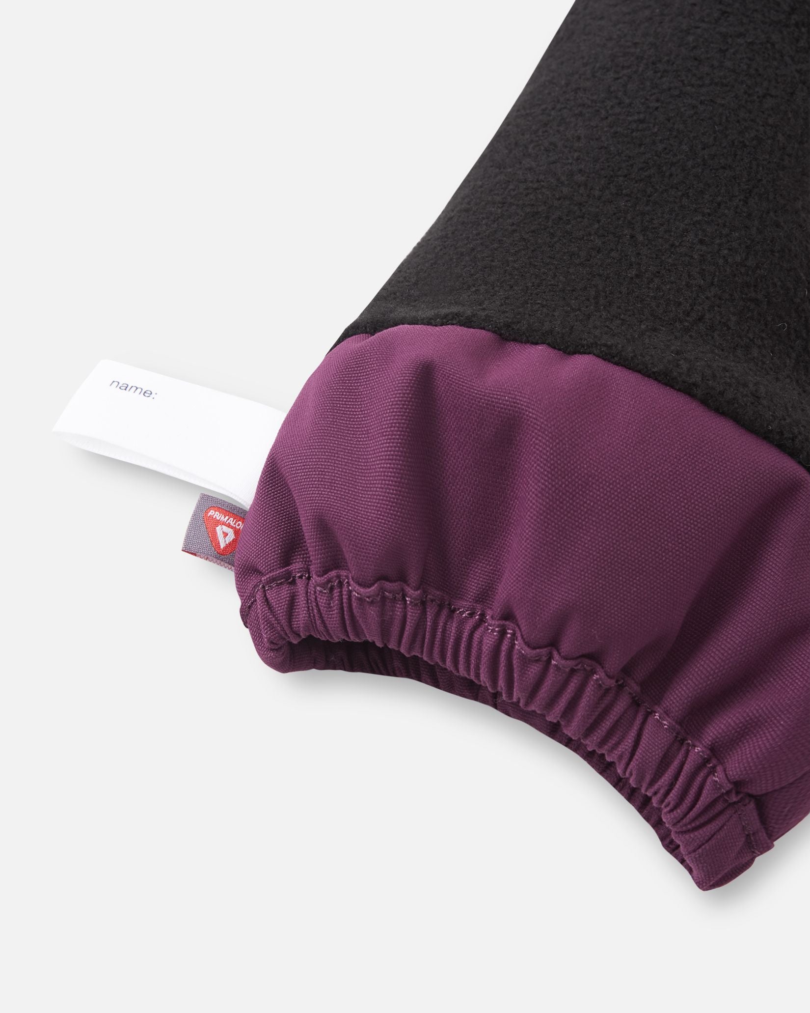 Close-up of the inner cuff on the deep purple Reima Ote kids' winter mittens, displaying the cozy black fleece lining, an inner name tag, and a PrimaLoft insulation label indicating high-performance heat retention.