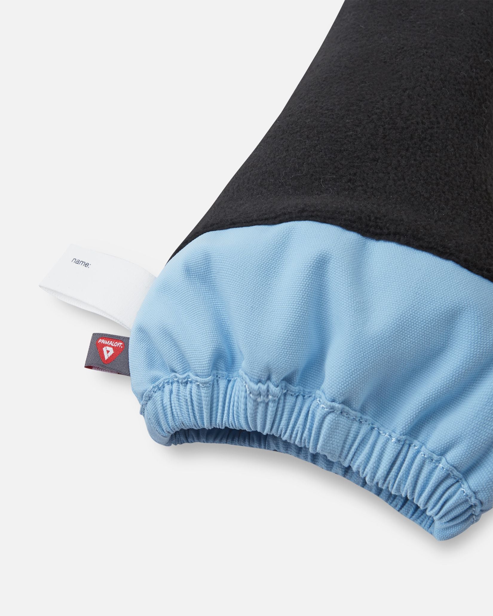 Inside cuff view of the frozen blue Reima Ote kids' winter mittens, highlighting the warm black fleece lining, a customizable name tag, and the premium PrimaLoft insulation tag for superior cold-weather thermal retention.