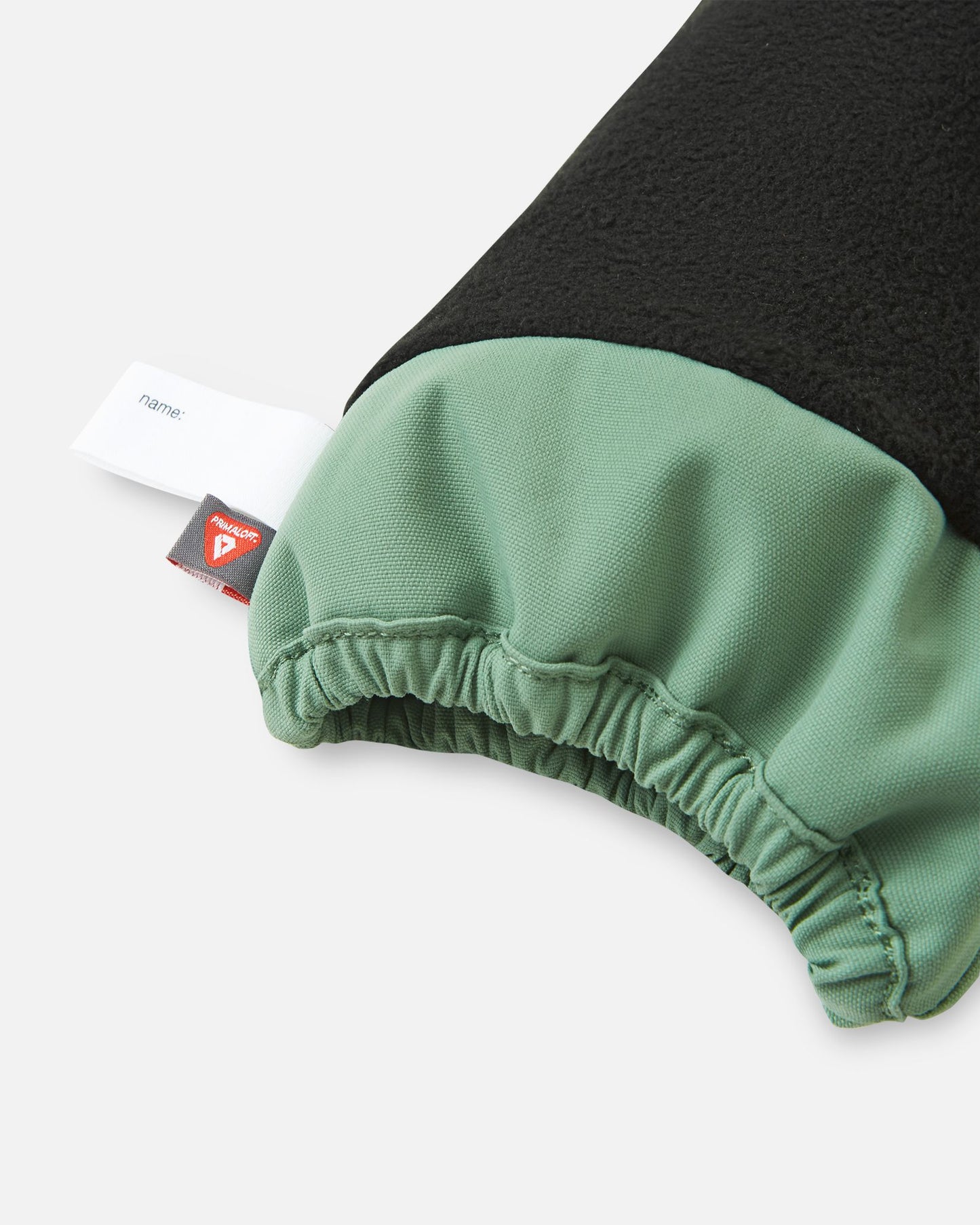 Inside cuff view of the green clay Reima Ote kids' winter mittens, highlighting the warm fleece lining, a customizable name tag, and the premium PrimaLoft insulation tag for superior cold-weather warmth.