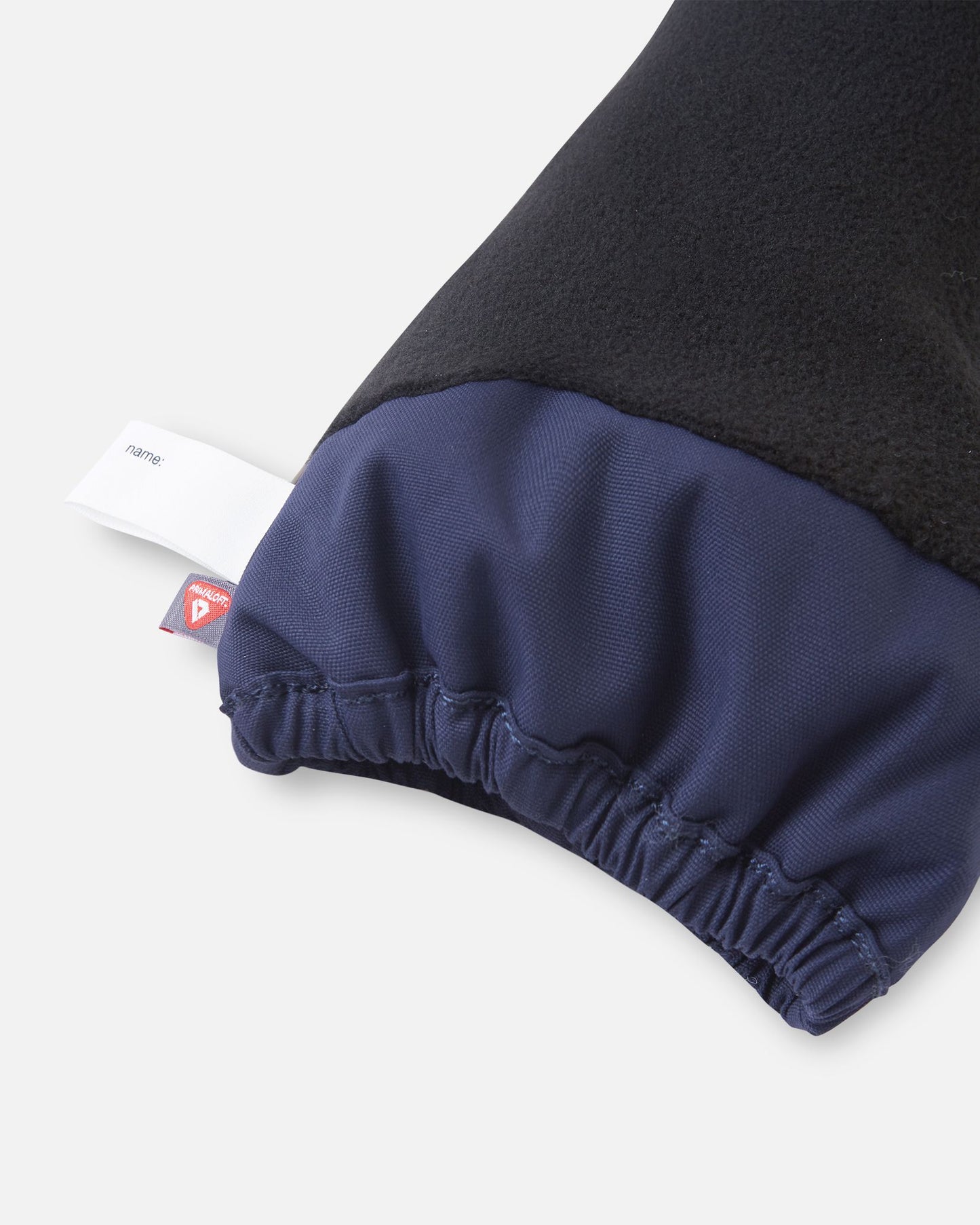 Close-up of the inner cuff on the navy blue Reima Ote kids' winter mittens, displaying the cozy black fleece lining, an inner name tag, and a PrimaLoft insulation label indicating high-performance thermal heat retention.