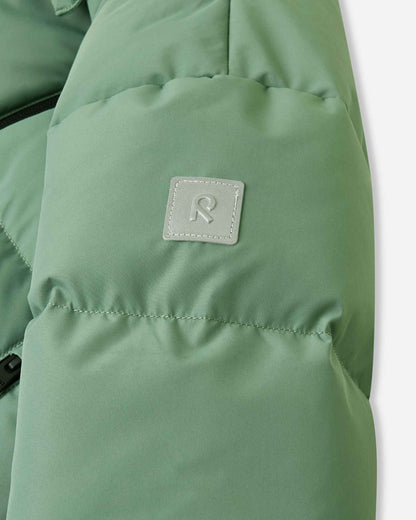 Close-up of the sleeve on the green clay Reima Paimio children's puffer coat, highlighting the square reflective Reima 'R' logo patch that enhances visibility during short winter days.