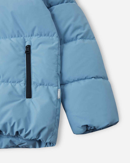Detailed close-up of the elastic sleeve cuff, lower hem, and secure vertical zippered hand pocket on the cloudy blue Reima Paimio children's down puffer jacket.