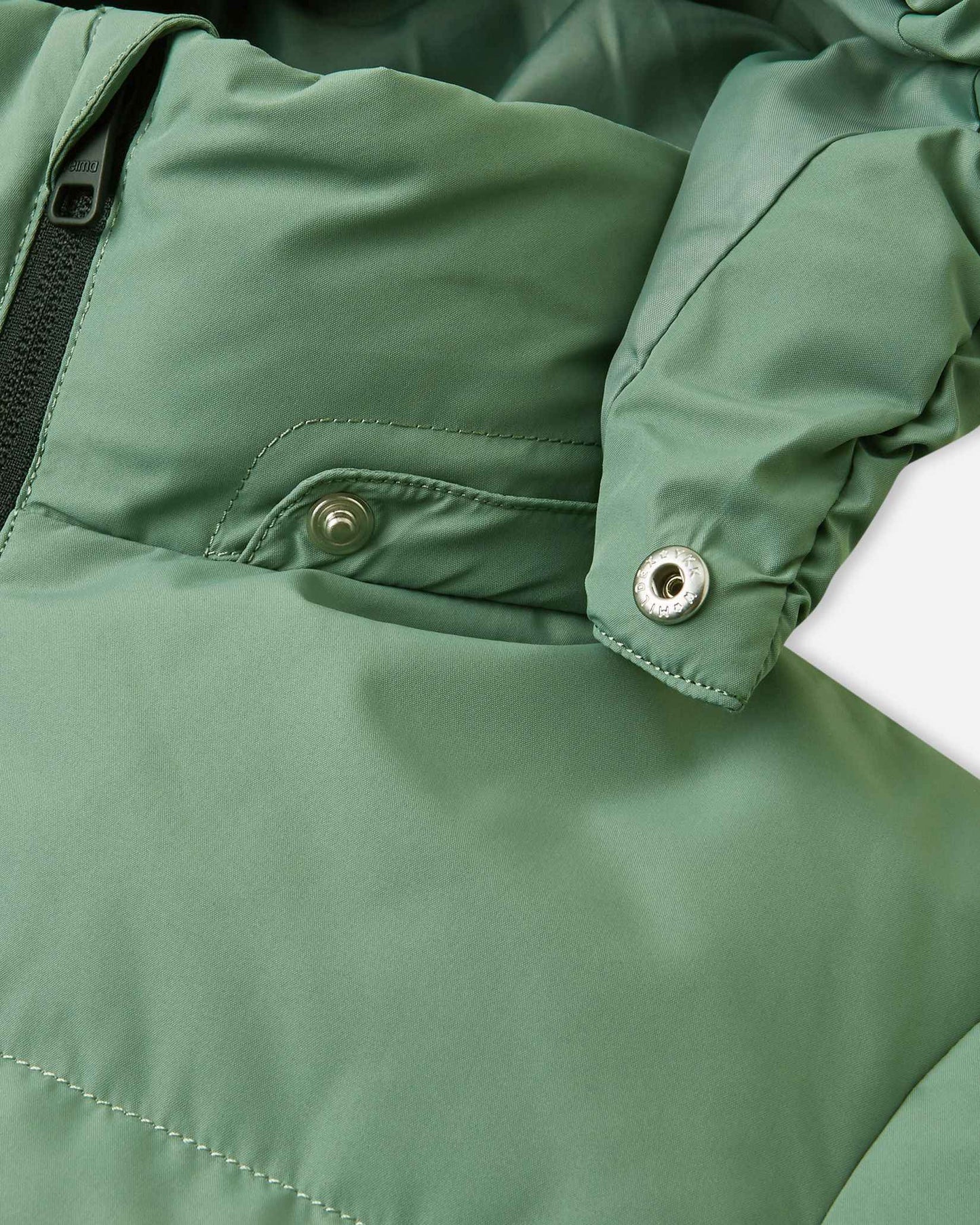 Detailed close-up of the disconnected metallic snap fastener on the collar of the green clay Reima Paimio kids' winter down jacket, demonstrating the safe, tear-away removable hood mechanism designed to easily release if snagged during active outdoor play.