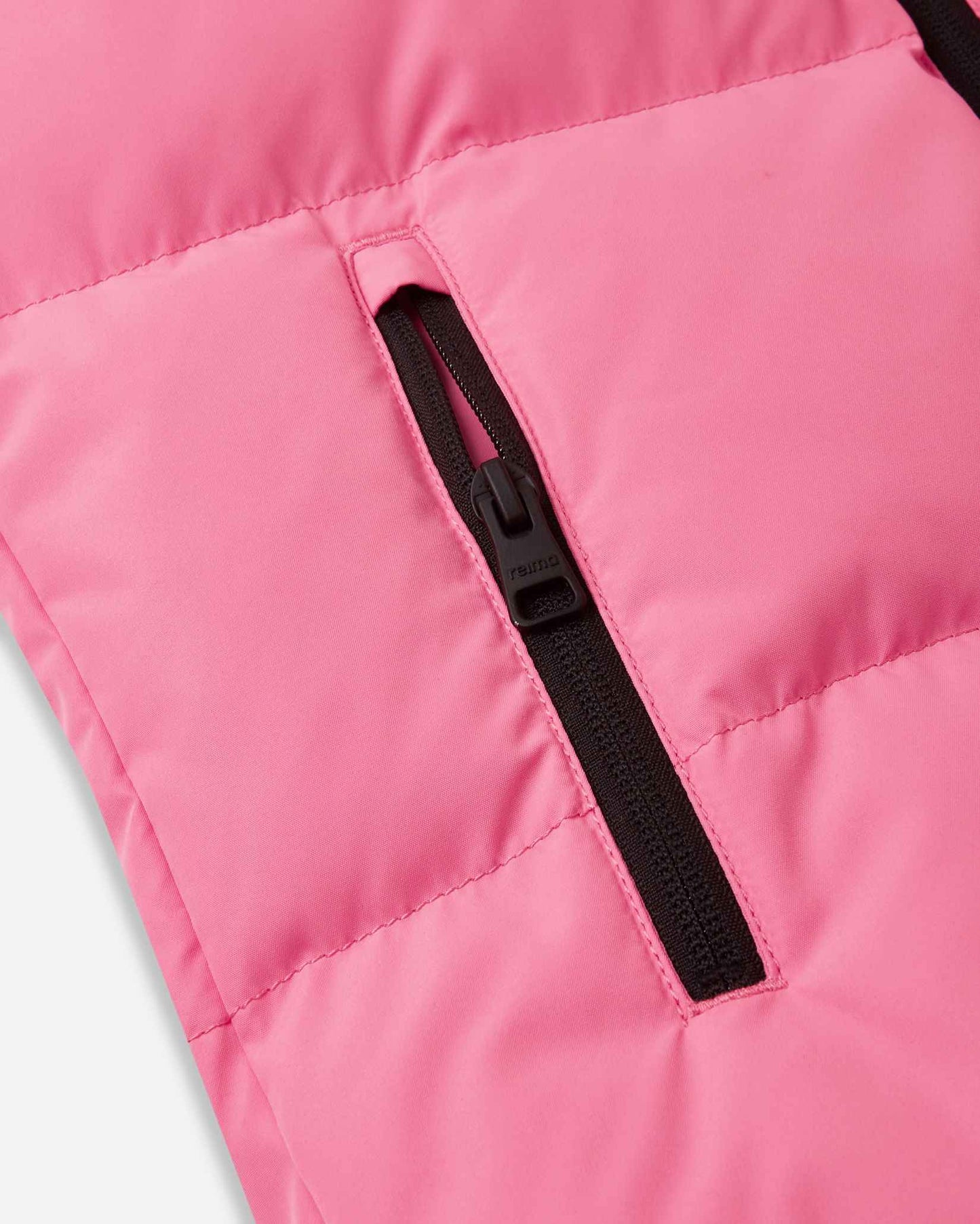 Close-up detail of the vertical side hand pocket on the soft coral Reima Paimio kids' winter coat, featuring a secure black zipper to keep small hands warm and essentials safe on the slopes.