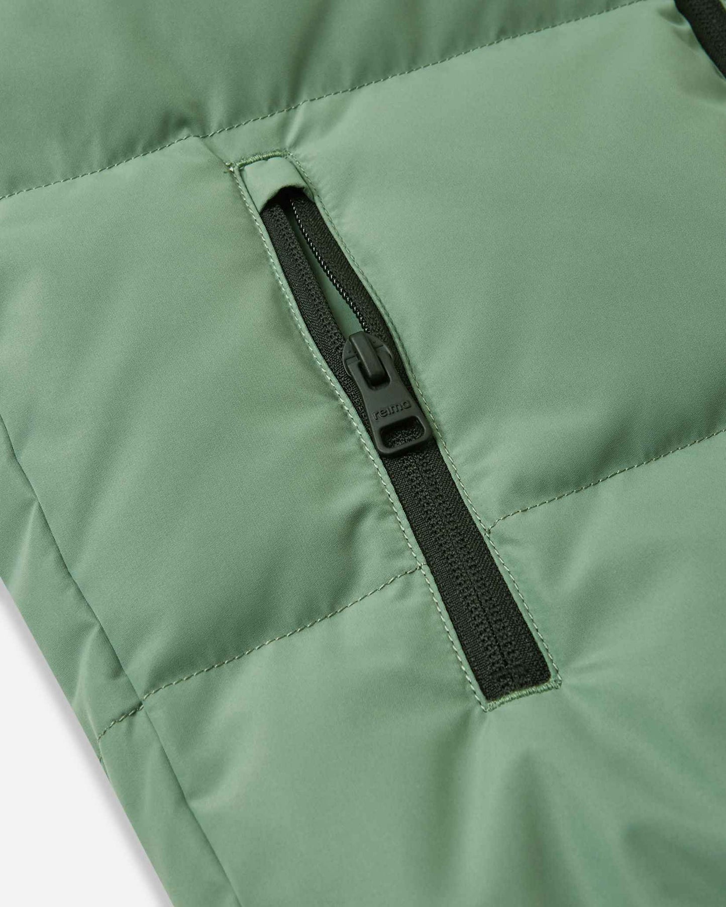 Close-up detail of the vertical side pocket on the green clay Reima Paimio kids' winter coat, featuring a secure black zipper to keep small hands warm and essentials safe.
