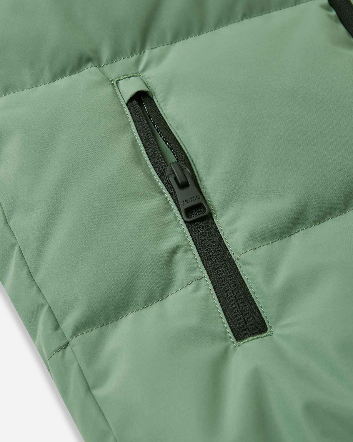 Close-up detail of the vertical side pocket on the green clay Reima Paimio kids' winter coat, featuring a secure black zipper to keep small hands warm and essentials safe.