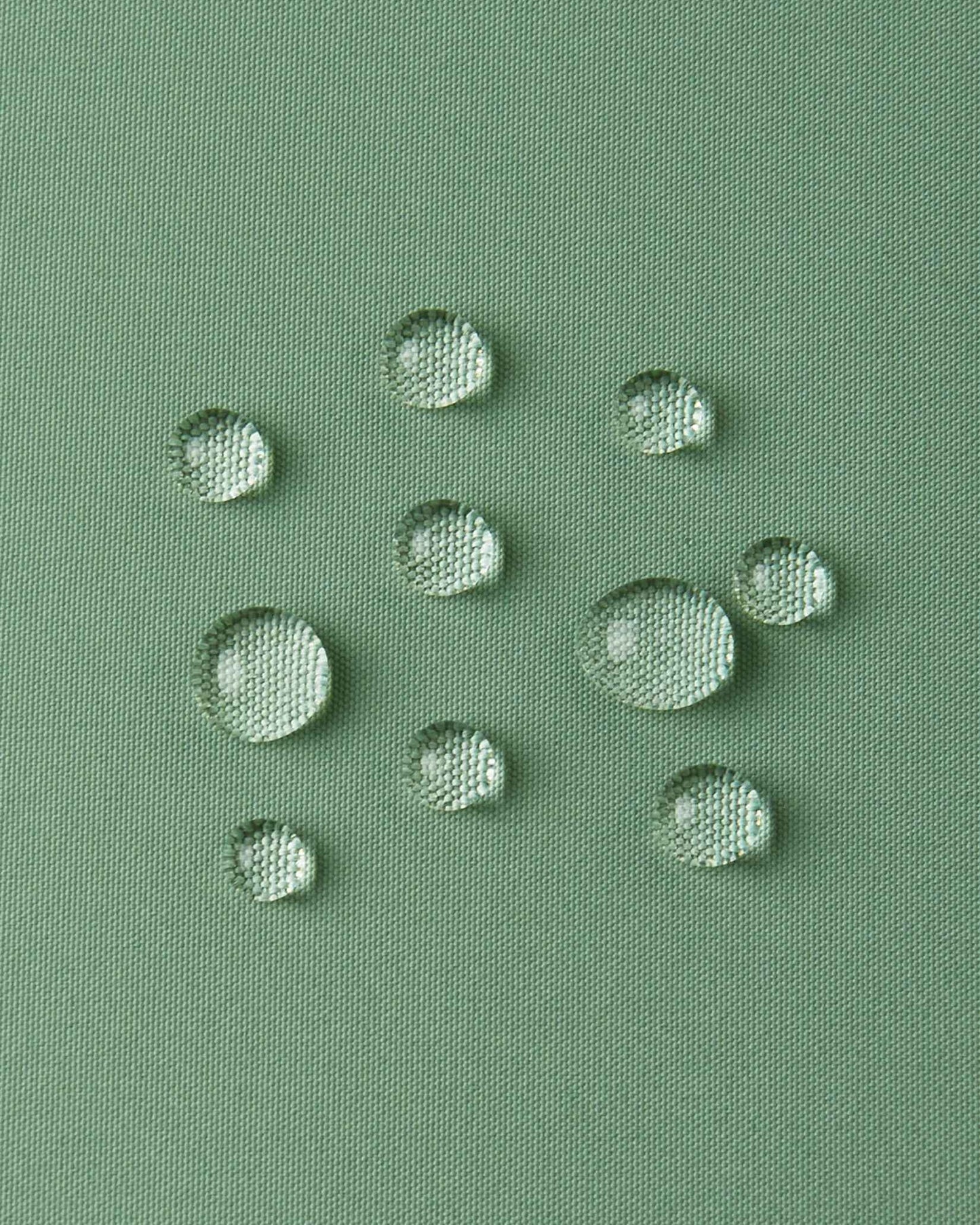 Macro close-up of water droplets forming beads on the green clay outer shell of the Reima Paimio jacket, illustrating the highly water-resistant, dirt-repellent, and breathable material.