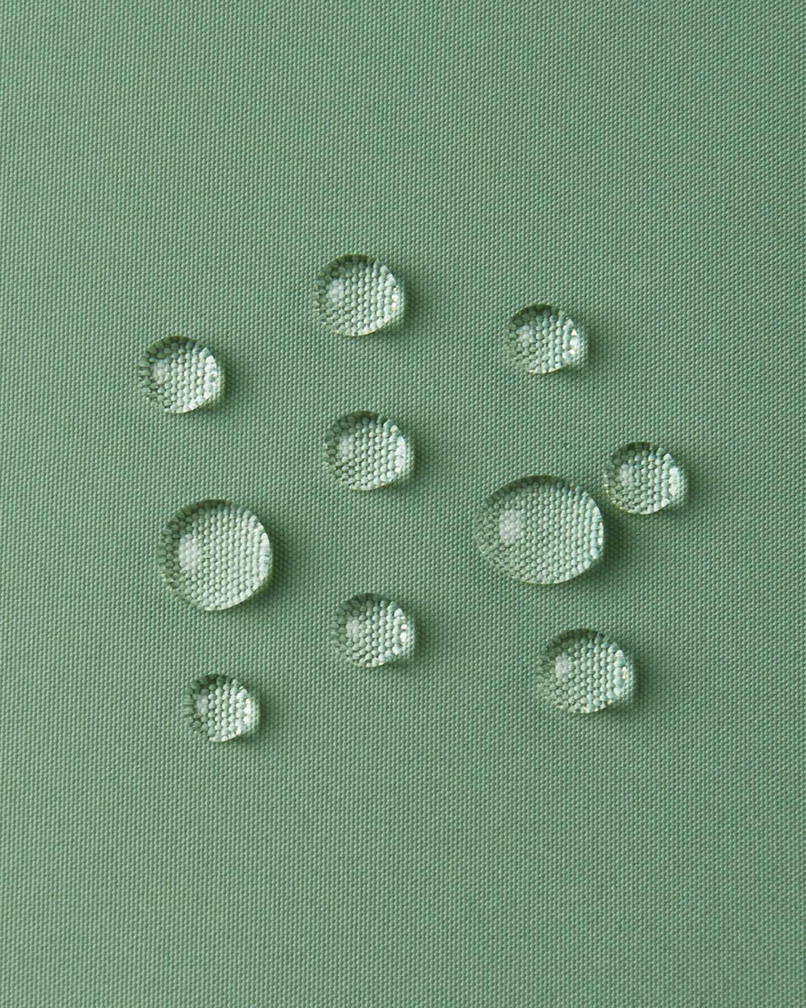 Macro close-up of water droplets forming beads on the green clay outer shell of the Reima Paimio jacket, illustrating the highly water-resistant, dirt-repellent, and breathable material.