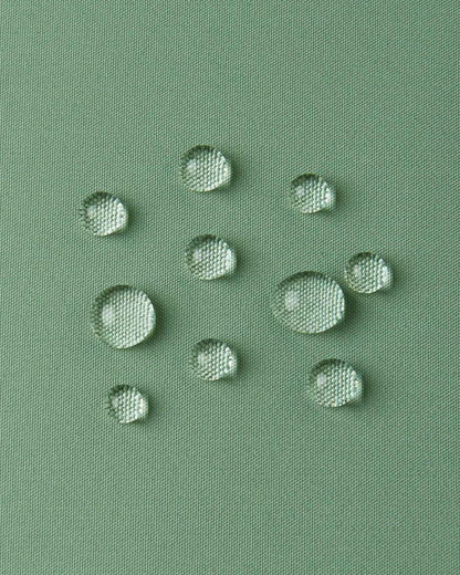 Macro close-up of water droplets forming beads on the green clay outer shell of the Reima Paimio jacket, illustrating the highly water-resistant, dirt-repellent, and breathable material.