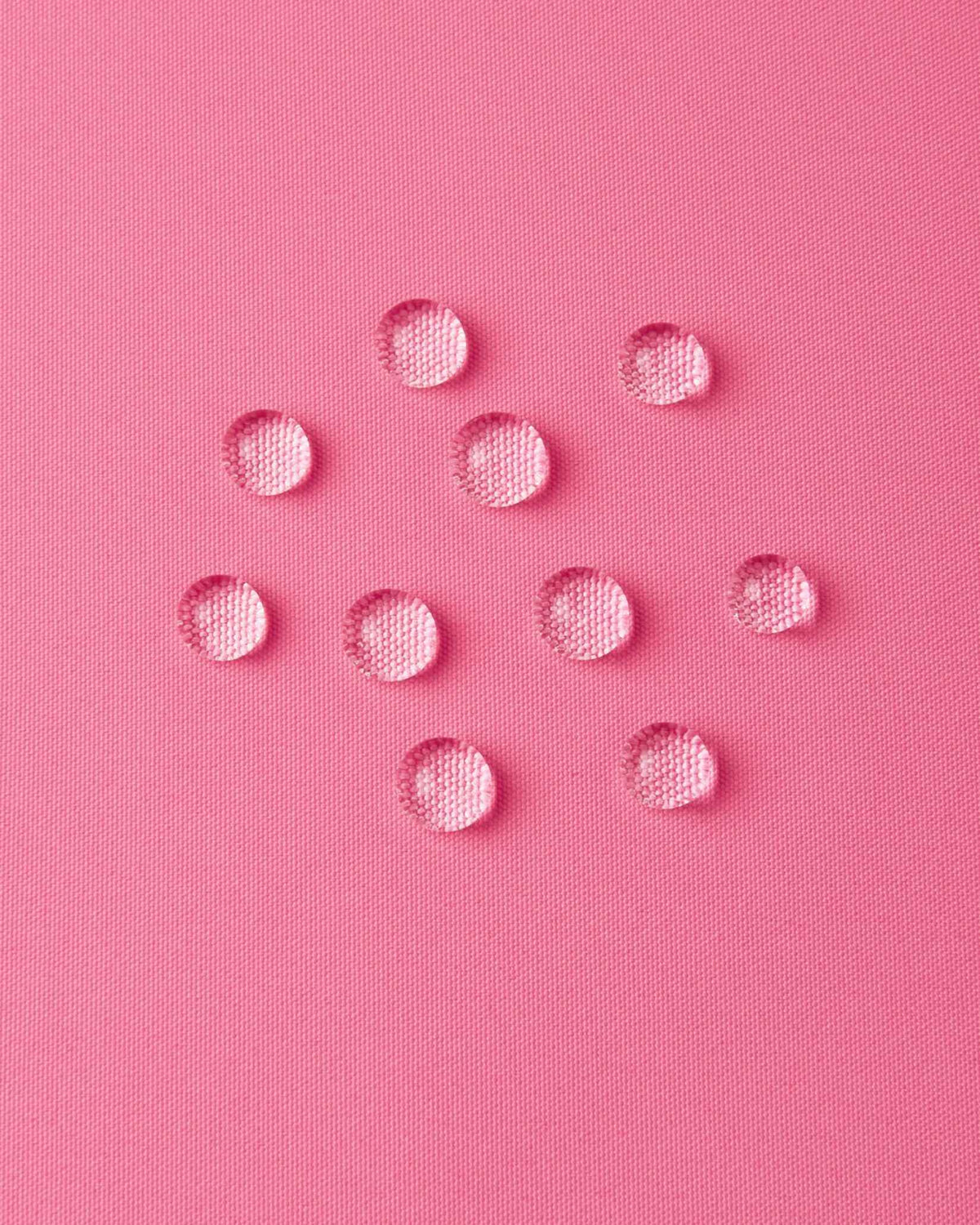 Macro close-up of water droplets forming beads on the soft coral pink outer shell of the Reima Paimio jacket, illustrating the highly water-resistant, dirt-repellent, and breathable material.