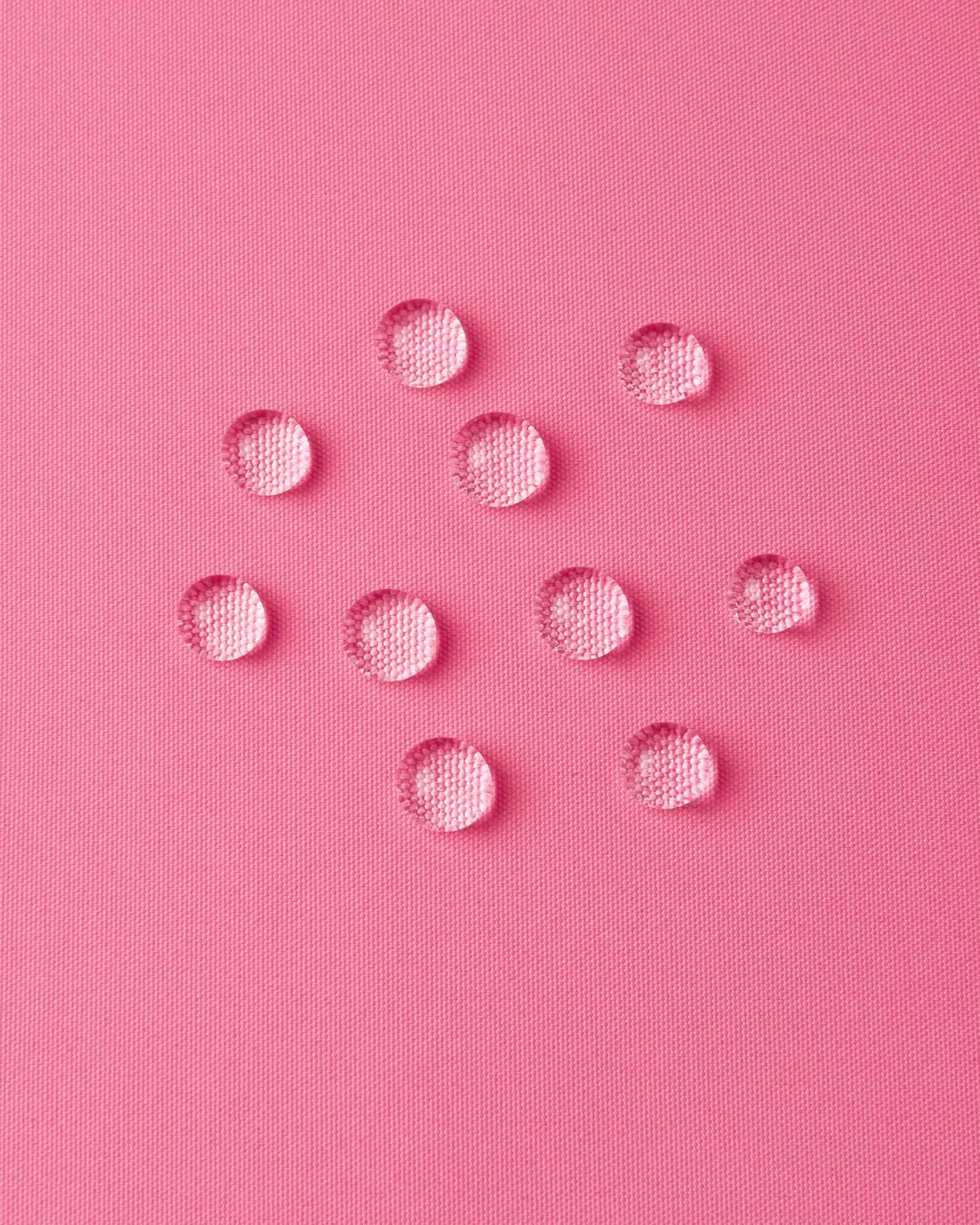 Macro close-up of water droplets forming beads on the soft coral pink outer shell of the Reima Paimio jacket, illustrating the highly water-resistant, dirt-repellent, and breathable material.