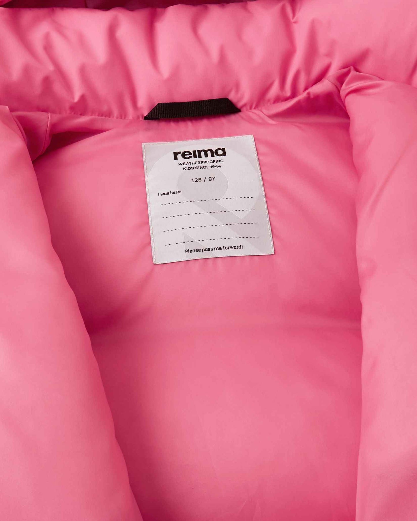 Inside view of the Reima Paimio youth winter jacket in soft coral, displaying the Reima weatherproofing label, sizing information, and a customizable "I was here" name tag block for school or winter camp.